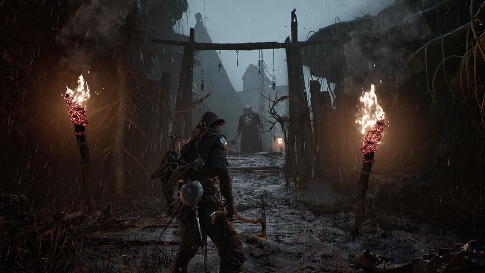 Rain-soaked warrior advances down a torch-lit muddy path toward a robed foe beneath a wooden gate. — Mortal Shell II screenshot